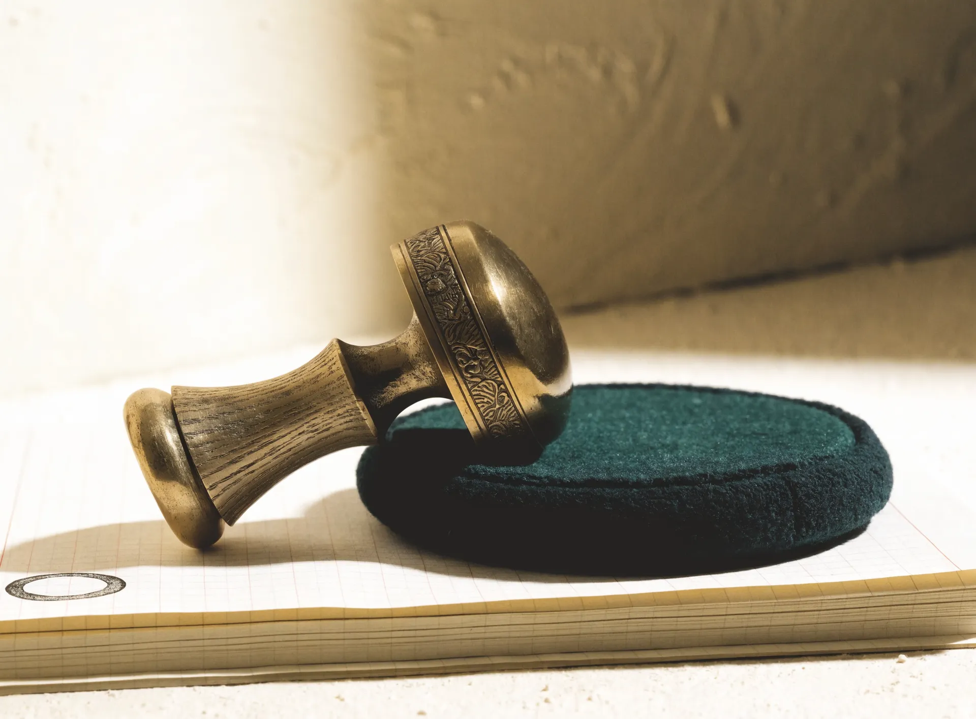 An antique brass approval seal resting on a spruce ink pad over ledger stock, beside one stamped ring